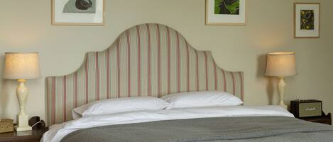 A neatly made bed with a striped headboard, two bedside lamps, and framed artwork on the wall.