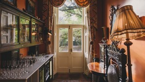 A room with a wooden floor, a bar area with glasses, a door leading outside, and a lamp. - Ballyvolane House (Kilcor)
