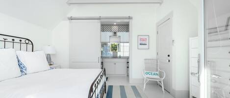 A bedroom with a bed, a nightstand, a chair, a wardrobe, and a bathroom visible through an open door.