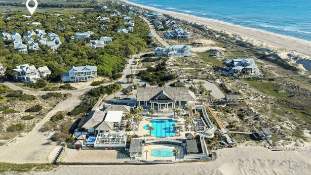 Une vue aérienne d’une propriété située sur la côte, avec plusieurs maisons, une grande piscine et une plage.