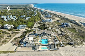 An aerial view of a coastal property with multiple houses, a large swimming pool, and a beach.