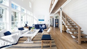 Un vaste salon aux couleurs blanche et bleue, un coin repas et un escalier en bois.