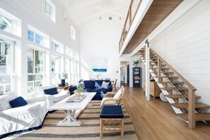 A spacious living room with a white and blue color scheme, a dining area, and a wooden staircase.