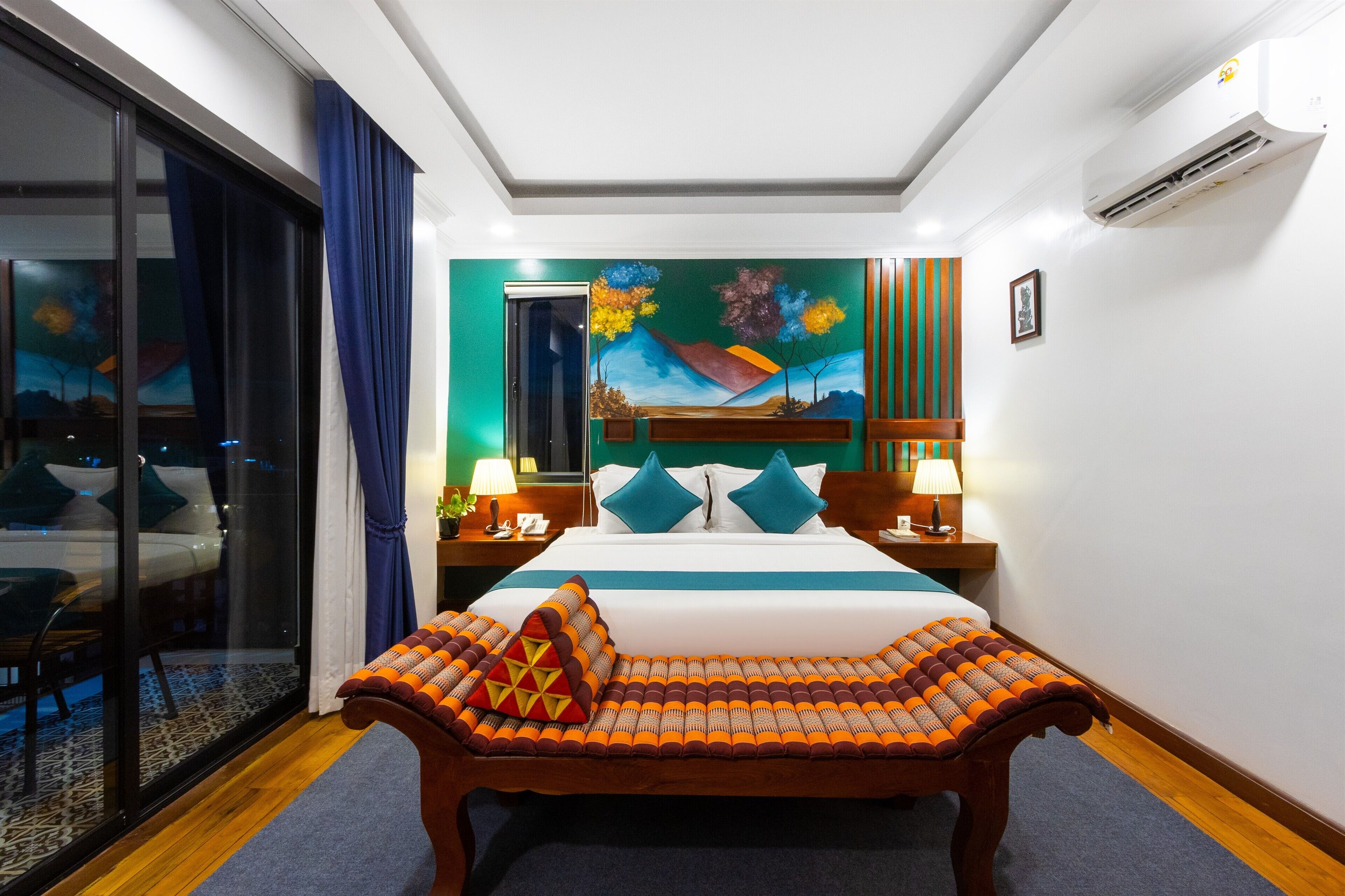 Ein Hotelzimmer mit einem großen Bett, einer Holzbank, einem Gemälde an der Wand und Blick durch eine Glastür.
