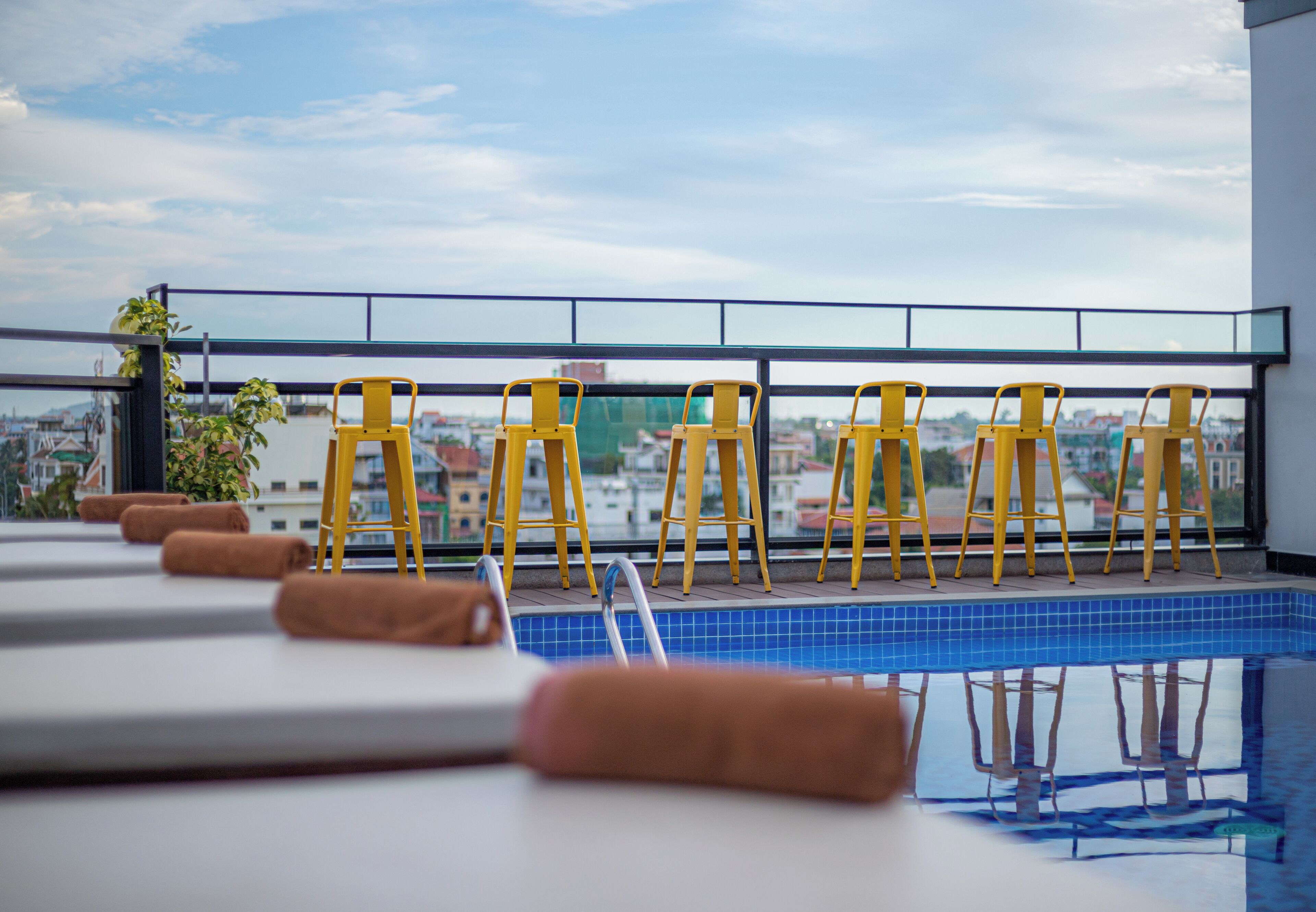 Area piscina sul tetto con sedie e asciugamani gialli, vista sulla città.