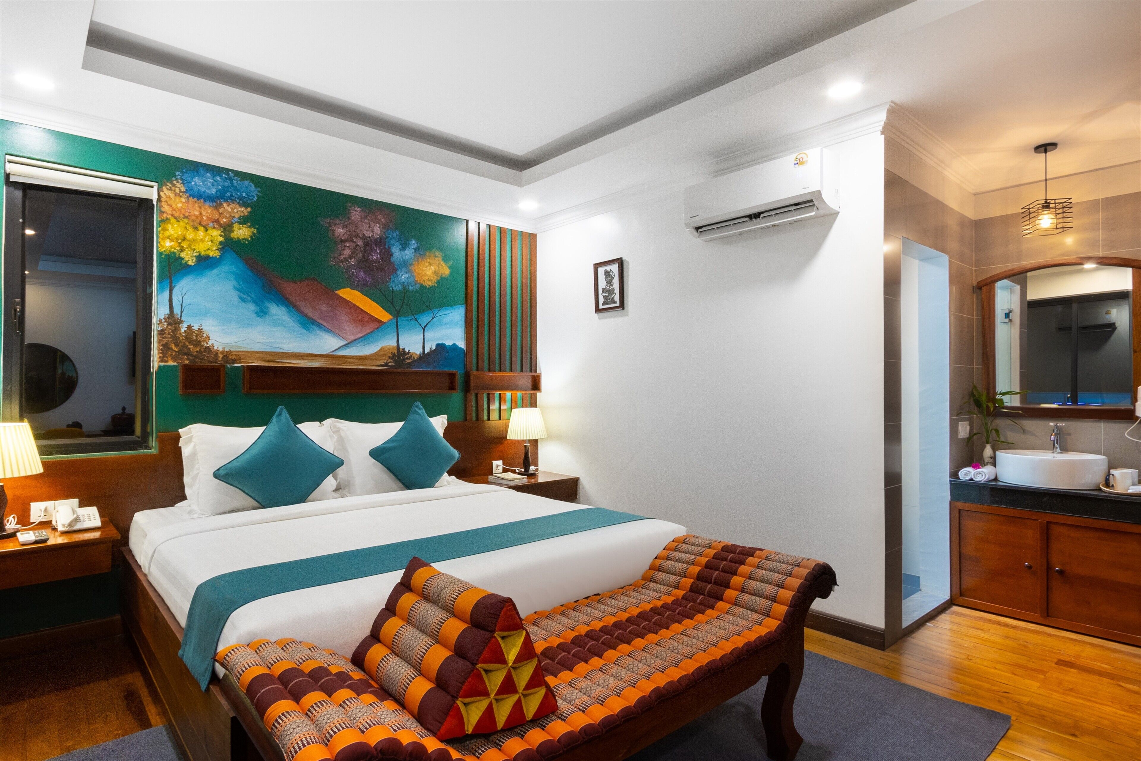 A hotel room with a large bed, a painting on the wall, a bathroom with a sink and mirror, and a wooden floor.