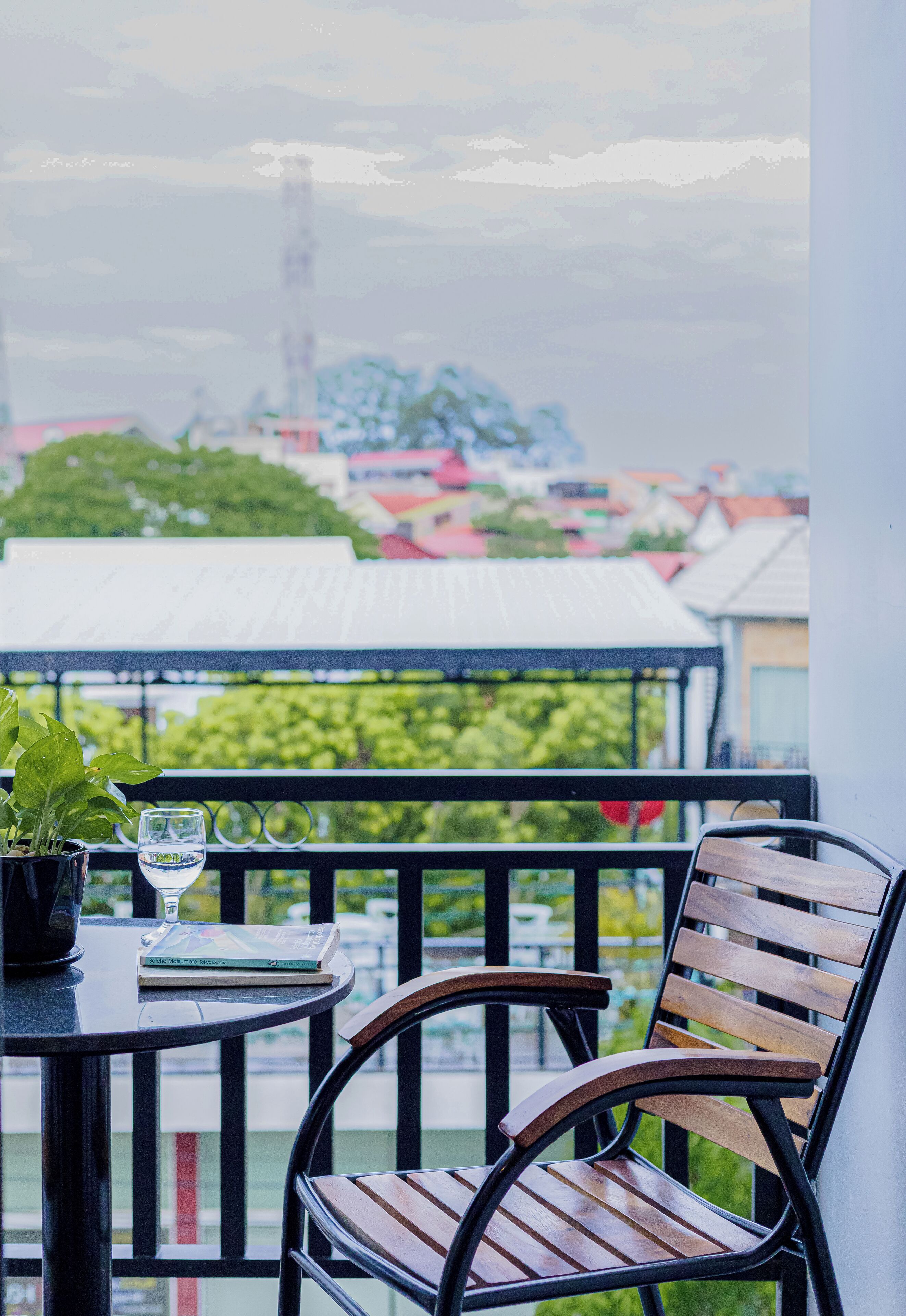 A balcony with a wooden chair, a table with a book and a glass of water, and a potted plant.