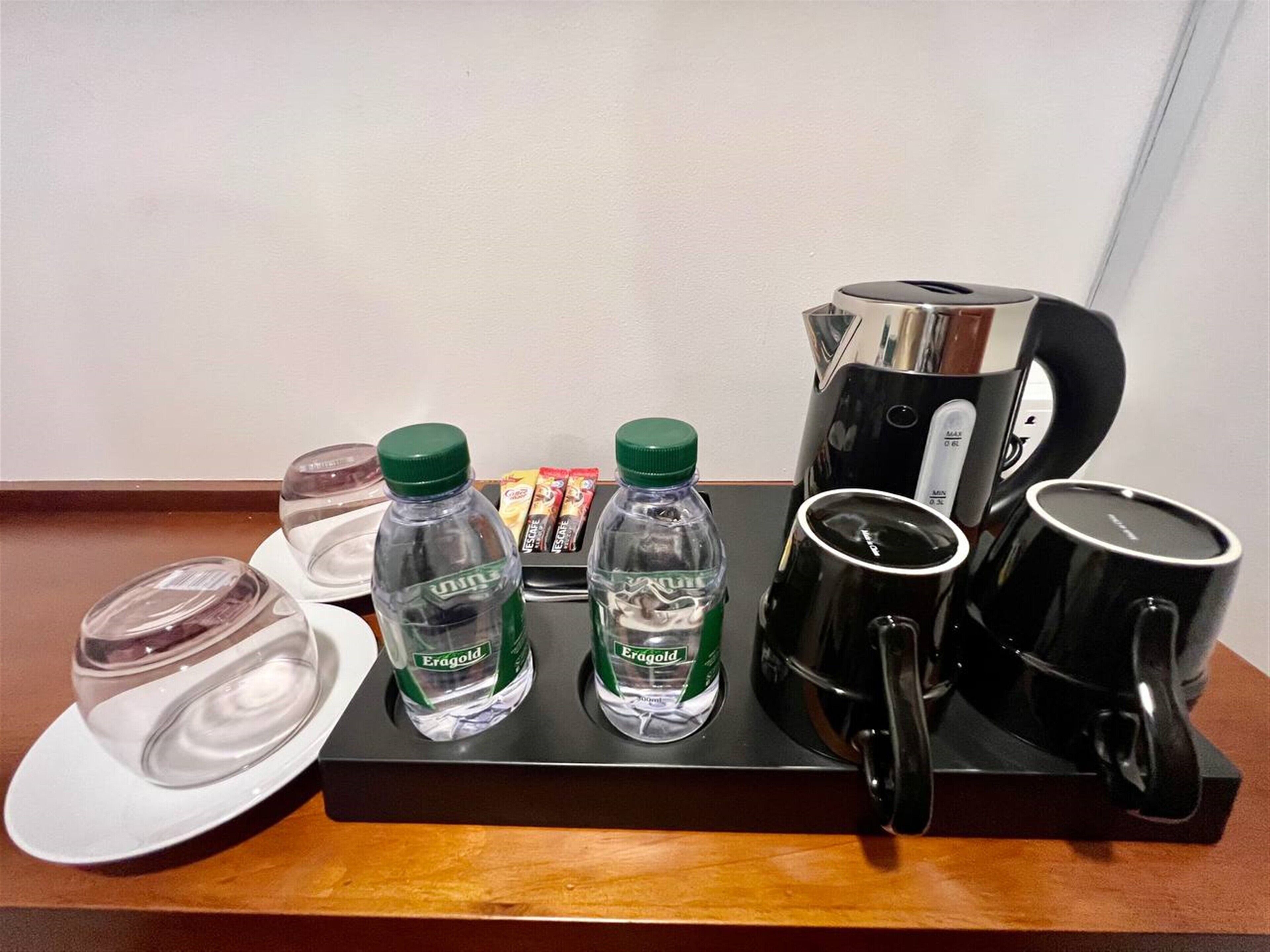 A tray with two Eragold water bottles, a coffee maker, two black mugs, a glass, and a plate with a lid.