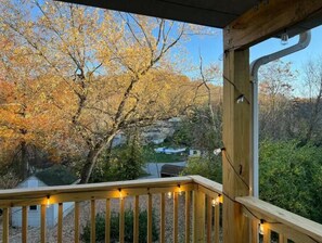 Eine Holzterrasse mit Lichterketten, mit Blick auf ein Tal mit herbstlich gefärbten Bäumen und ein Haus im Hintergrund.
