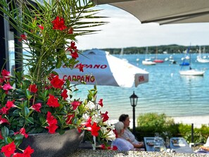 Un restaurante costero con terraza, vistas al puerto deportivo y un paraguas grande con el nombre 'CARPANO'.