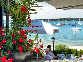 Restaurante à beira-mar com mesas ao ar livre e vista para o porto, e um grande guarda-sol com o nome "CARPANO".