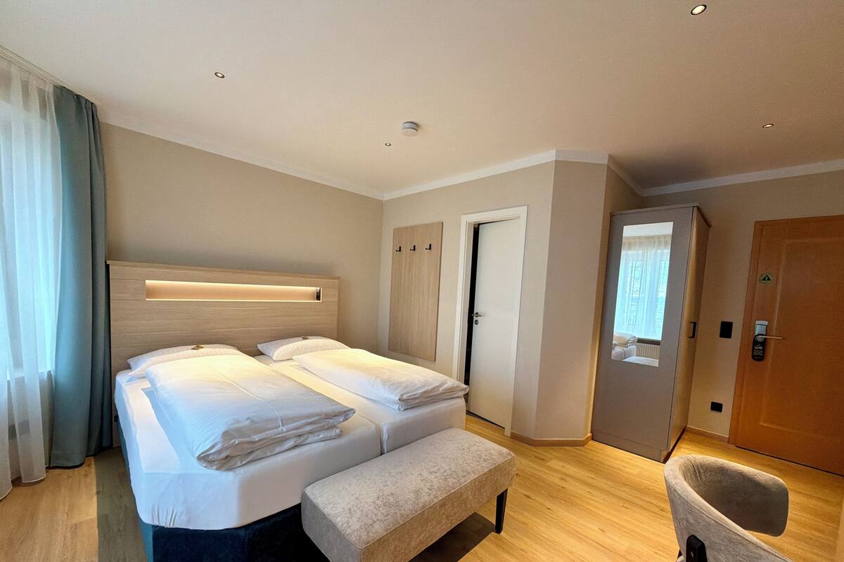 A hotel room with a large bed, a bench, a desk, and a chair.