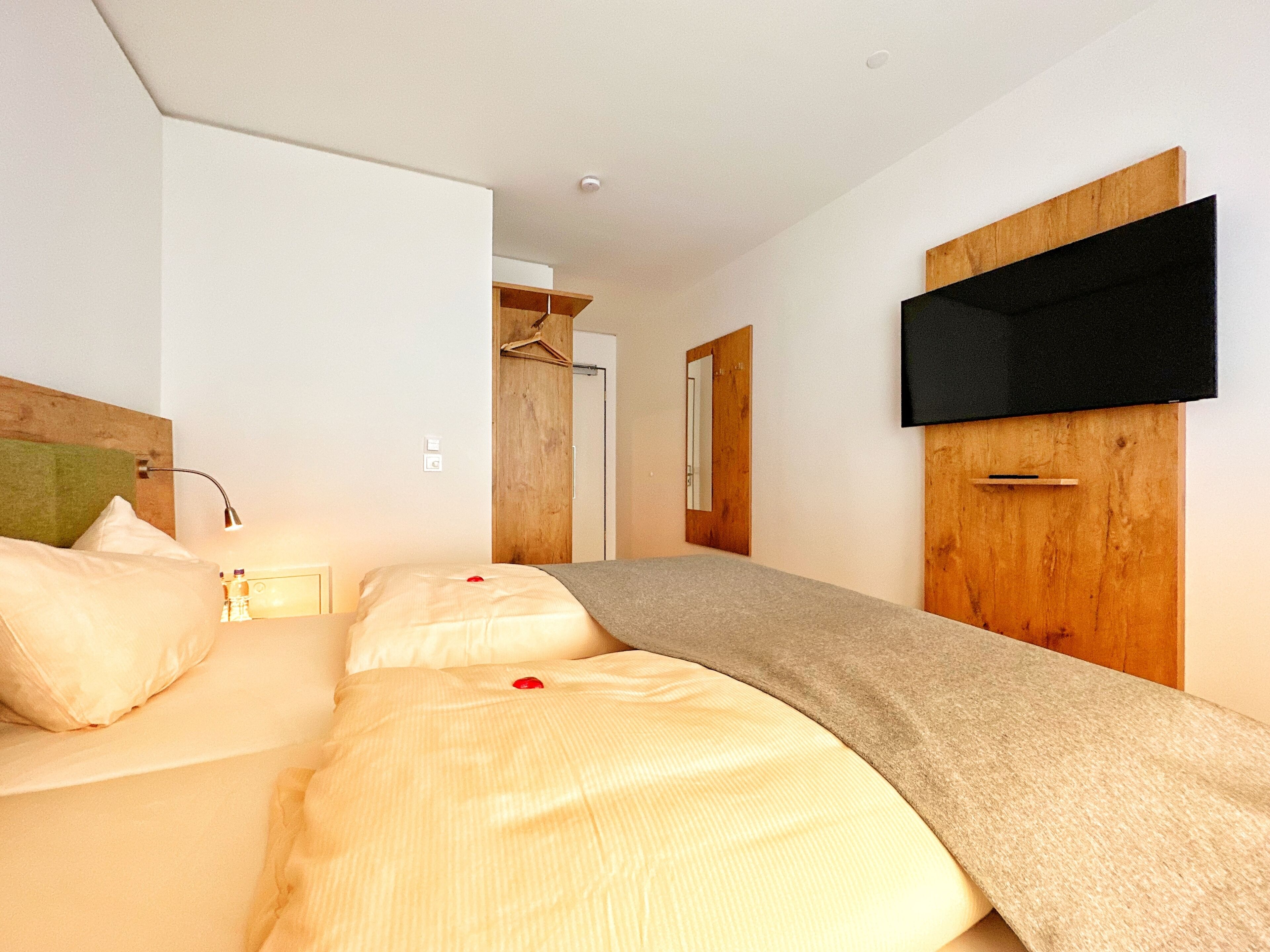 Una habitación de hotel moderna con cama, mesita de noche, lámpara y televisor montado en la pared.