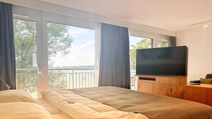 Une chambre d’hôtel avec un lit, un téléviseur posé sur un meuble en bois et un balcon donnant sur la mer.