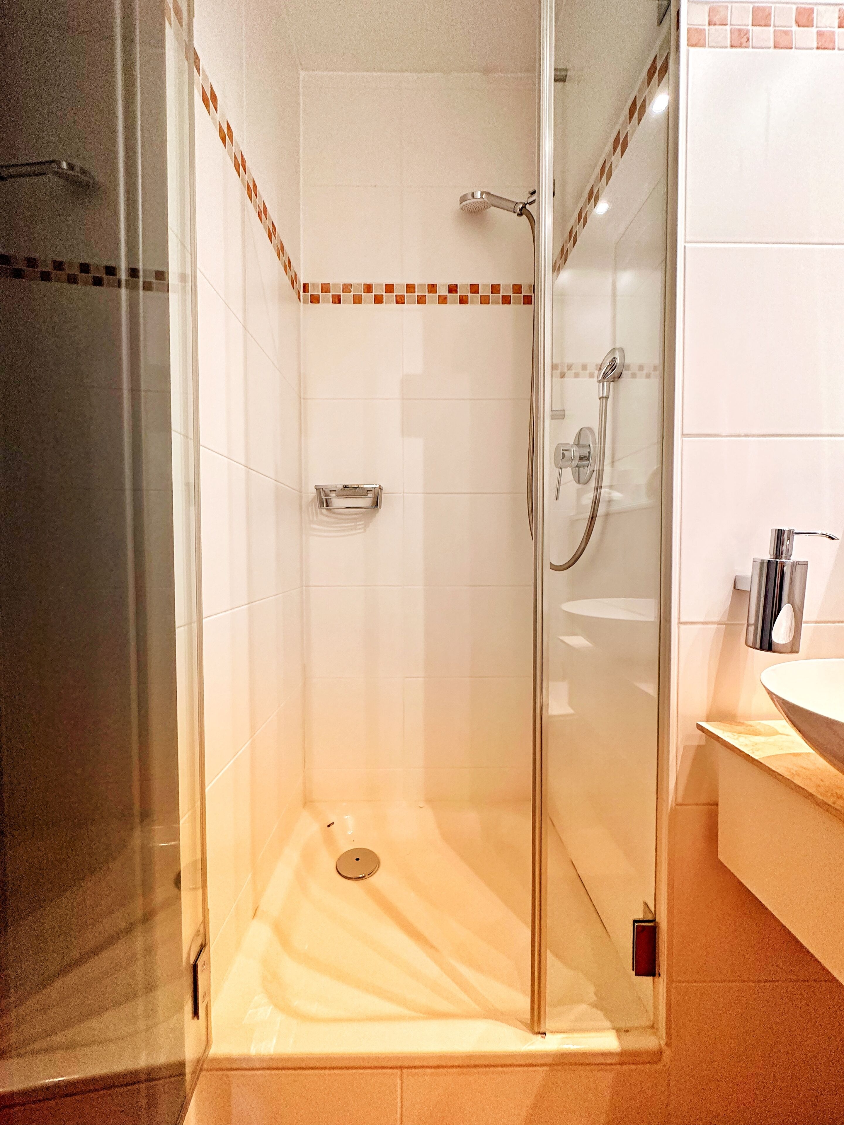 Une douche fermée par des parois de verre, avec un mur recouvert de carreaux, un porte-serviettes et un lavabo doté d’un plan de travail.