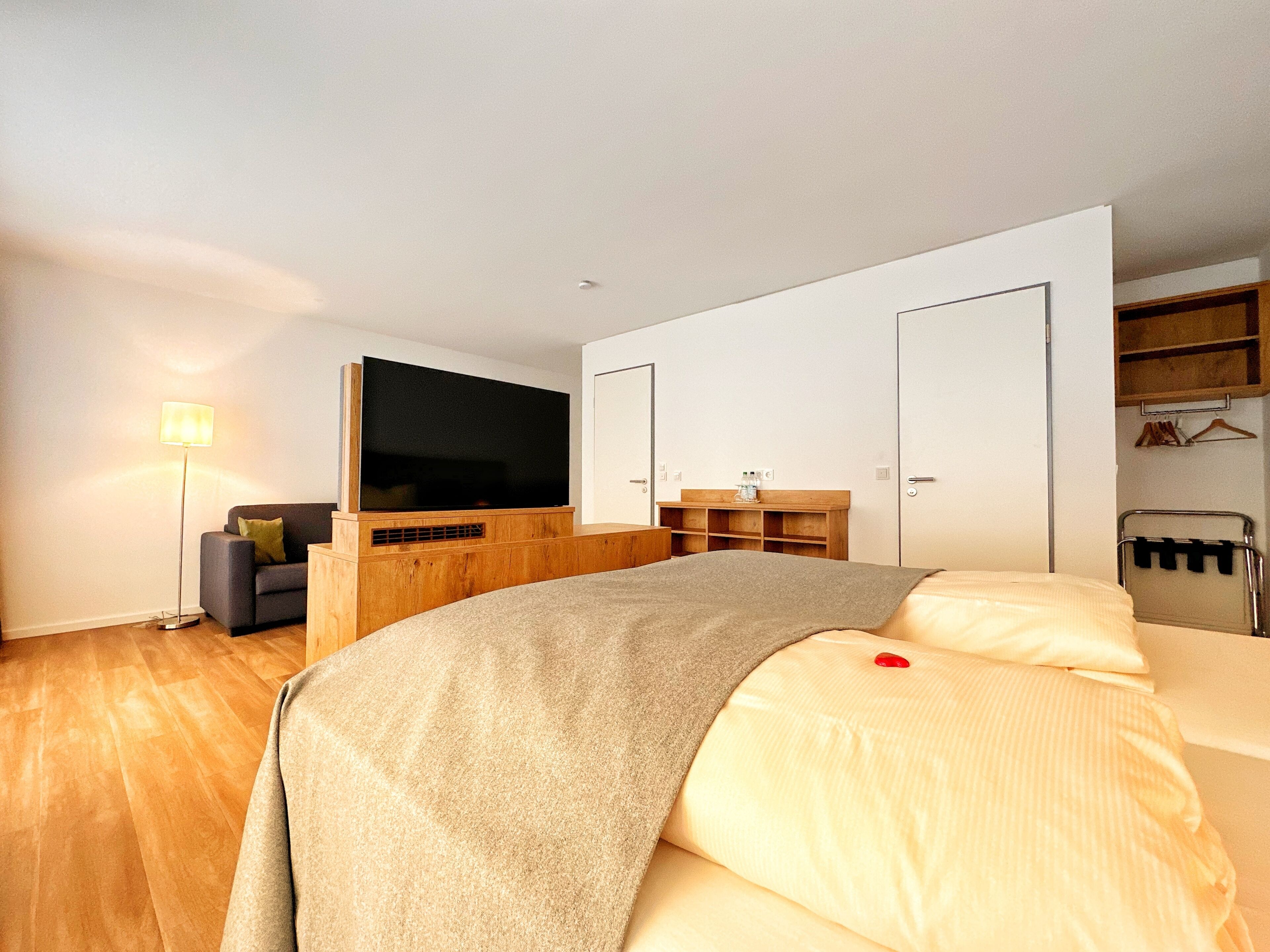Un dormitorio moderno con una cama grande, un televisor de pantalla plana, una mesita de noche de madera, un estante junto a la cama y un armario.