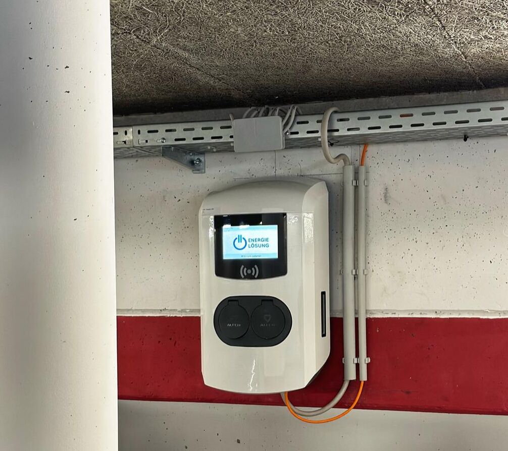 Un parking avec une borne de recharge blanche fixée au mur.