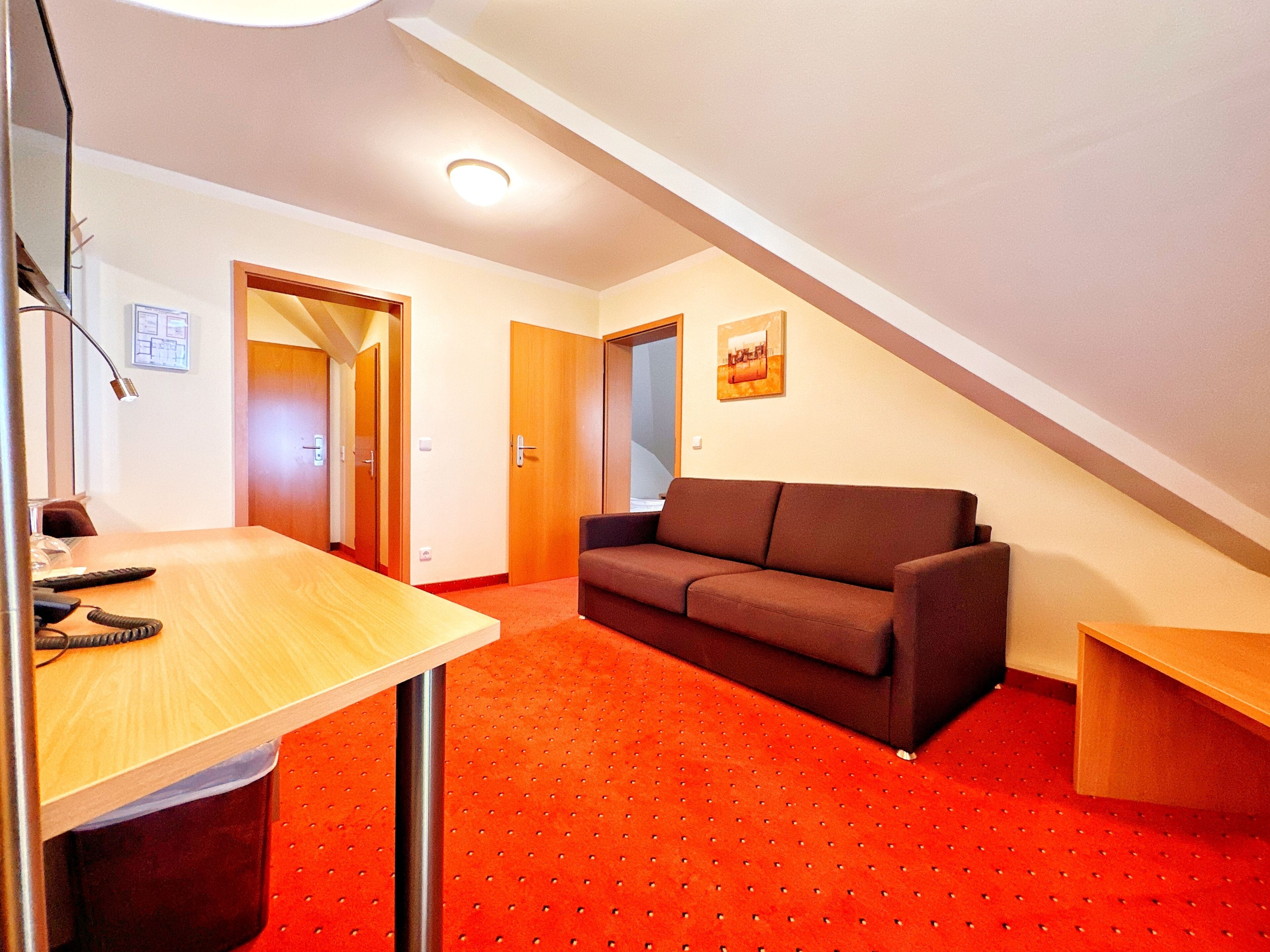 A room with a wooden desk, a brown sofa, and a red carpet.