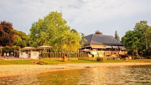 Un bâtiment situé au bord du lac, doté d’une terrasse, entouré d’arbres et bordé d’une zone sablonneuse.