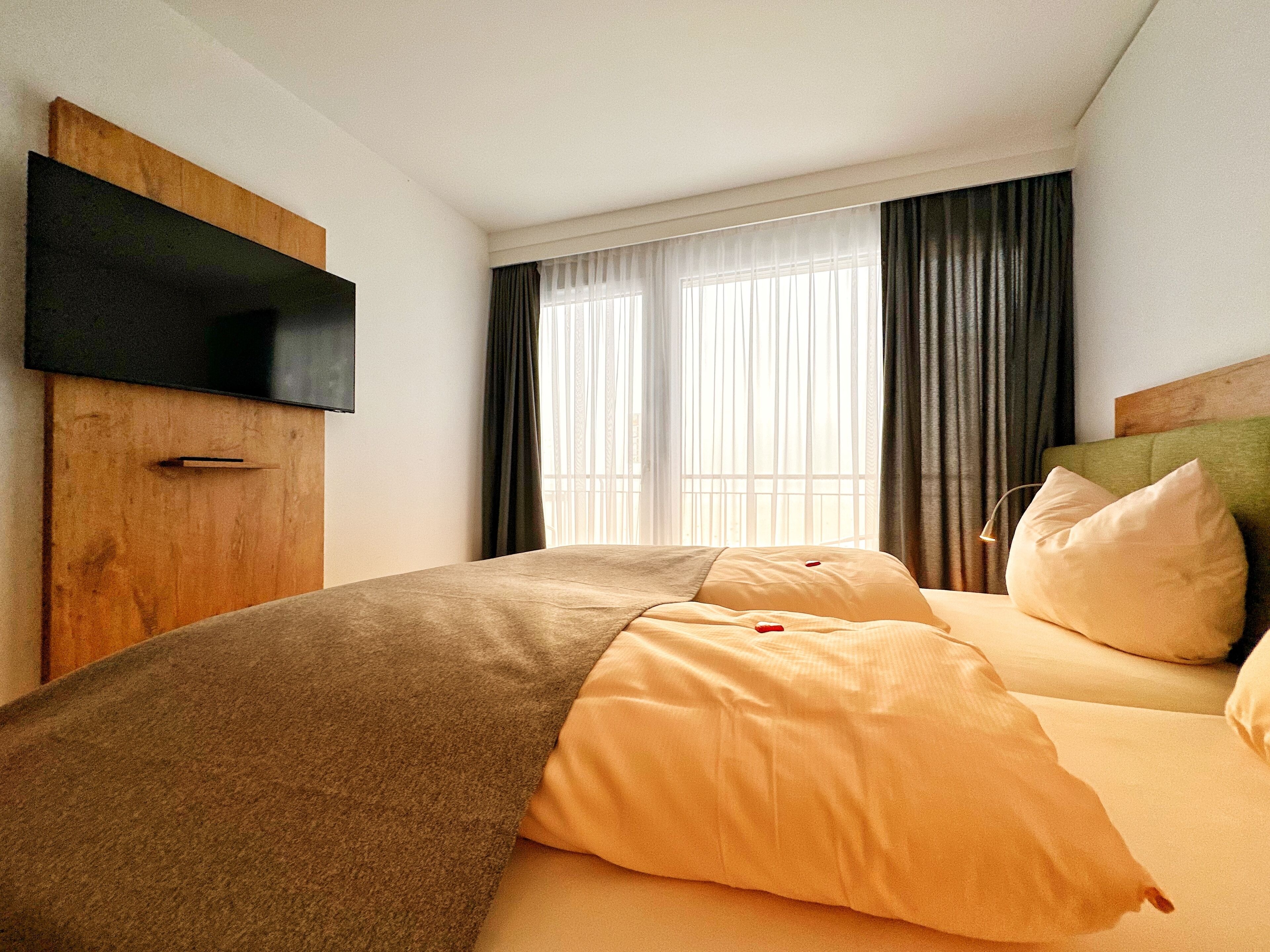 Ein Hotelzimmer mit Bett, Wandfernseher und einem Vorhangfenster.