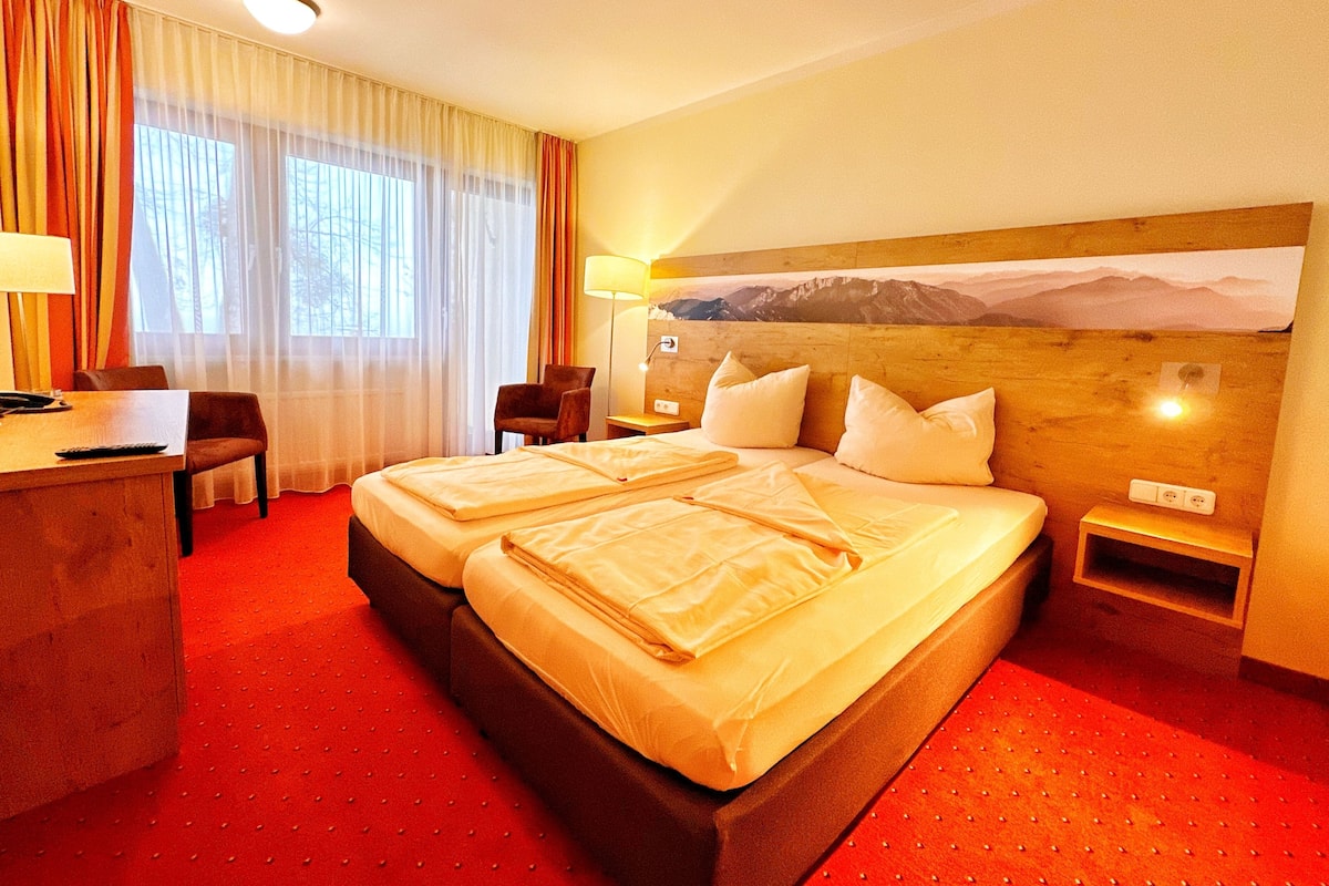 A hotel room with a large bed, a desk with a chair, a lamp, and a painting on the wall.