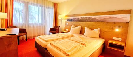 Ein Hotelzimmer mit einem großen Bett, einem Schreibtisch mit Stuhl, einer Lampe und einem Bild an der Wand.
