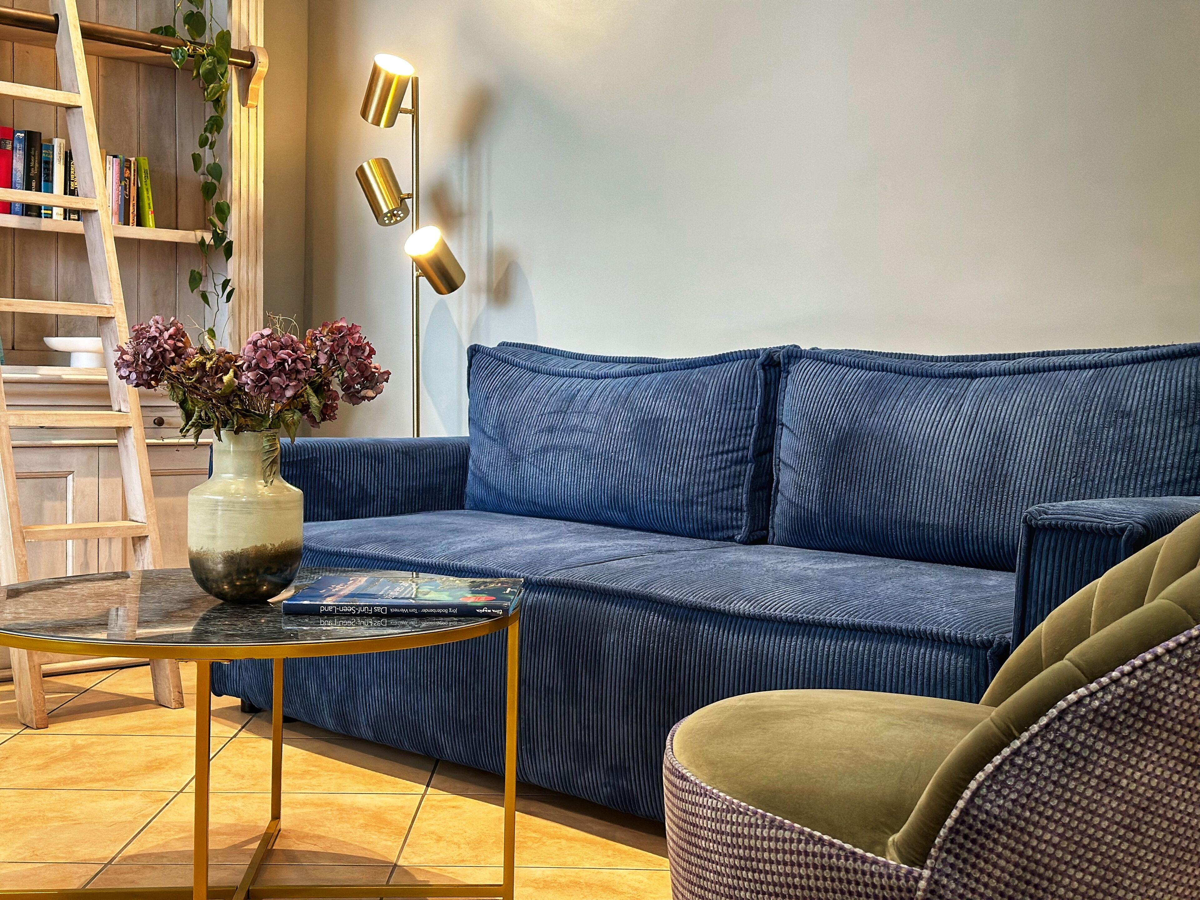 A living room with a blue sofa, a small round table, a bookshelf, and a floor lamp.