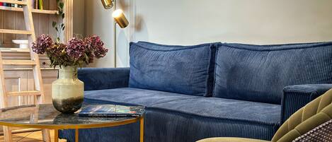 A living room with a blue sofa, a small round table, a bookshelf, and a floor lamp.