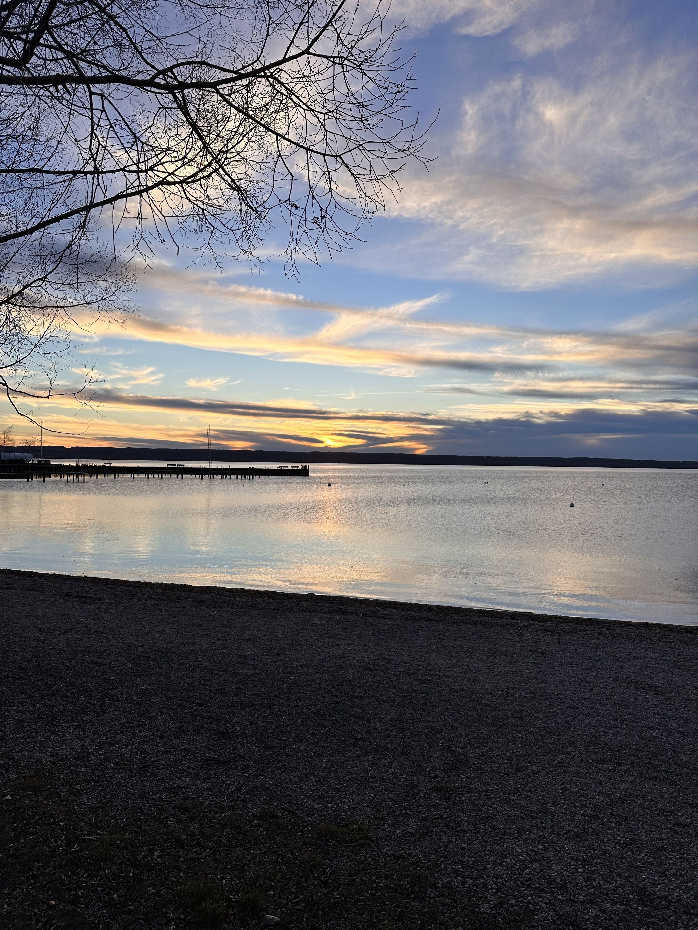 Un lac paisible, avec une jetée qui s’avance sur l’eau, entouré d’arbres sans feuilles et sous un ciel dégagé.