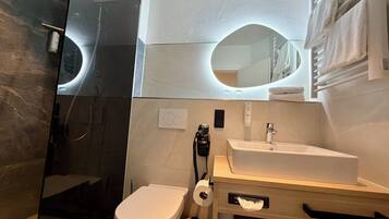 A modern bathroom with a glass shower enclosure, a white toilet, a sink with a mirror, and a towel rack.