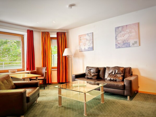A modern living room with a glass coffee table, leather sofa, and a dining area with a table and chairs.