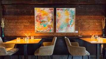 Un restaurant aux murs en bois, orné de deux tableaux abstraits, et dont la table est dressée avec des chaises et des verres.
