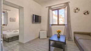 A modern hotel room with a bed, a small table with a vase, a TV, a window with curtains, and a sofa. - B&B il vagello (Florence)