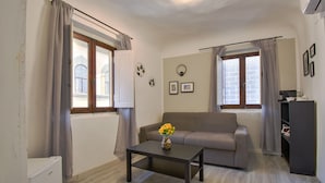 A living room with a sofa, a coffee table with a vase of flowers, a radiator, and a window with curtains. - B&B il vagello (Florence)