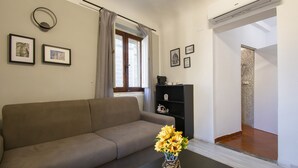 A living room with a sofa, a coffee table with a vase of flowers, a black bookshelf, and a window with curtains. - B&B il vagello (Florence)