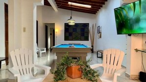 A pool table in a modern room with white chairs, a television, and a wooden ceiling.