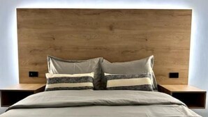 A modern bedroom with a wooden headboard, a large bed with multiple pillows, and two bedside tables.