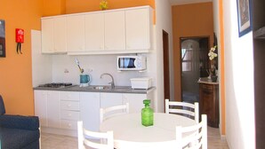 A compact kitchen with white cabinets, a microwave, and a gas stove. There is a dining table with chairs and a green bottle on it. - Casa da Horta, 1 bedroom apartment, CH1, Pool and Garden (Albufeira)