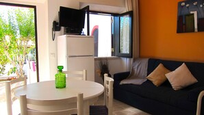 A living area with a white table, chairs, a dark blue sofa, and a television on a stand. - Casa da Horta, 1 bedroom apartment, CH1, Pool and Garden (Albufeira)