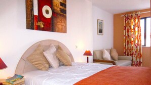 A hotel room with a large bed, a nightstand with a lamp, a chair, and a painting on the wall. - Casa da Horta, 1 bedroom apartment, CH1, Pool and Garden (Albufeira)