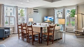 A modern living room with a dining area, large windows, a television, and a view of the cityscape. - Beautiful Inn, Lighthouse Landing. Sleeps 18-20 (Ogunquit)
