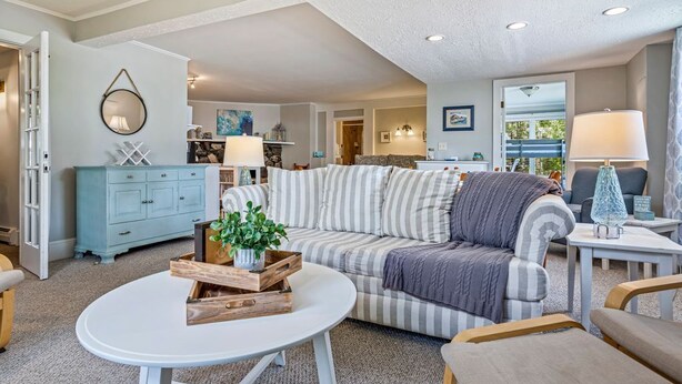 A cozy living room with a striped sofa, a round white table, and a blue cabinet. - Beautiful Inn, Lighthouse Landing. Sleeps 18-20 (Ogunquit)