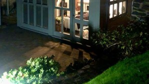 Une maison avec un toit en pente, de grandes fenêtres et un intérieur visible, où l’on aperçoit un lit et un chien.