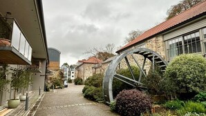 Une cour avec une roue à eau, des bâtiments en pierre et des plantes en pot.