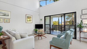 Un soggiorno moderno con divano, poltrone, tavolino e televisione. Alle pareti, quadri incorniciati e un balcone con vista.