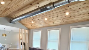 A modern living room with a wooden ceiling, a sectional sofa, a coffee table, and a dining area in the background. - Fully remodeled house in perfect location (Irons)