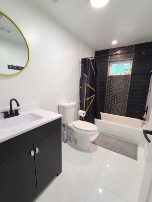 Un baño moderno con un lavamanos blanco, tocador negro, inodoro blanco y una bañera.