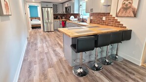 A modern kitchen with a wooden island and bar stools, a refrigerator, and a microwave. - Fully remodeled house in perfect location (Irons)