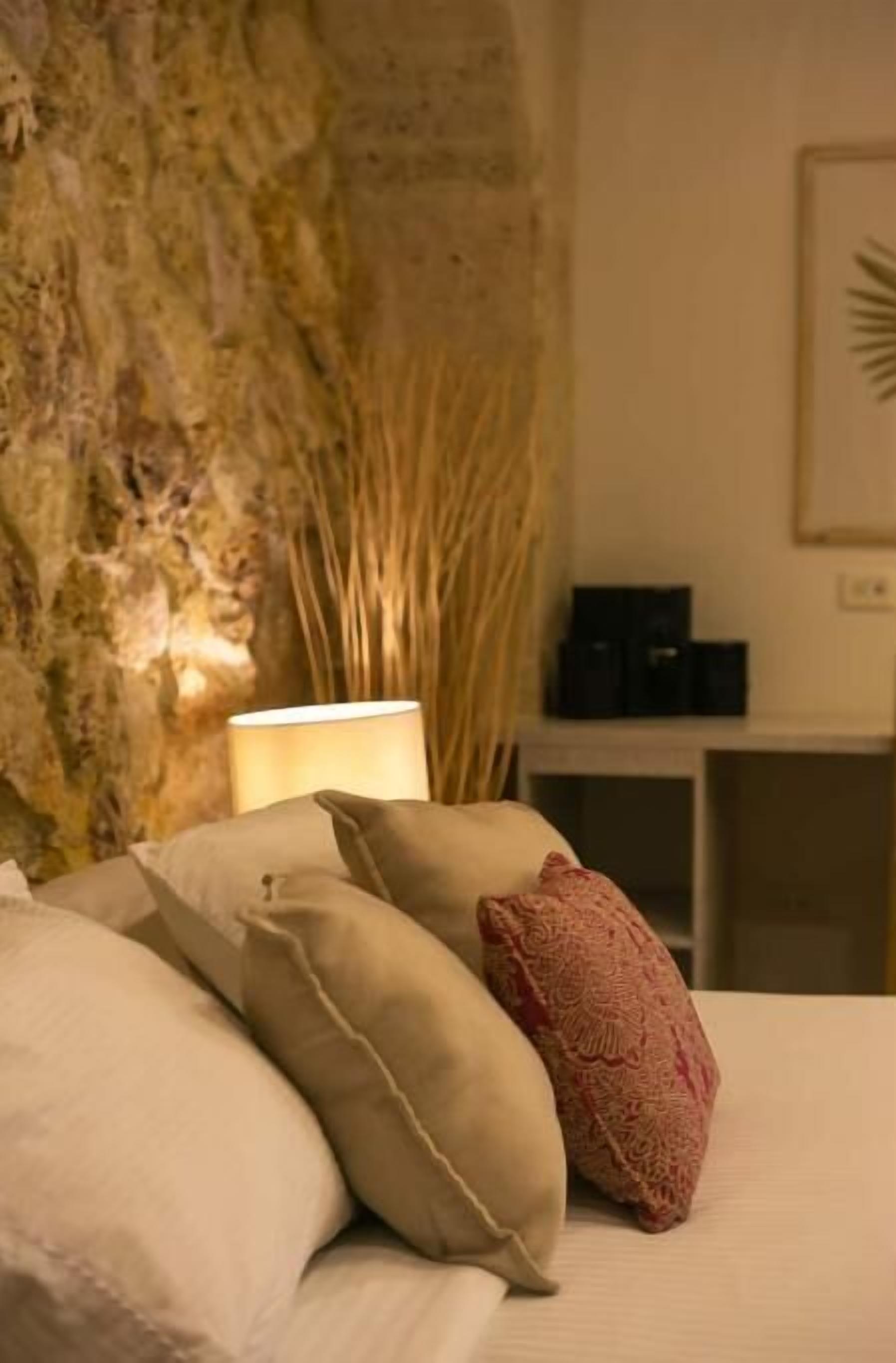 Camera da letto con parete in pietra, una lampada da comodino e un comodino con dispositivi elettronici.