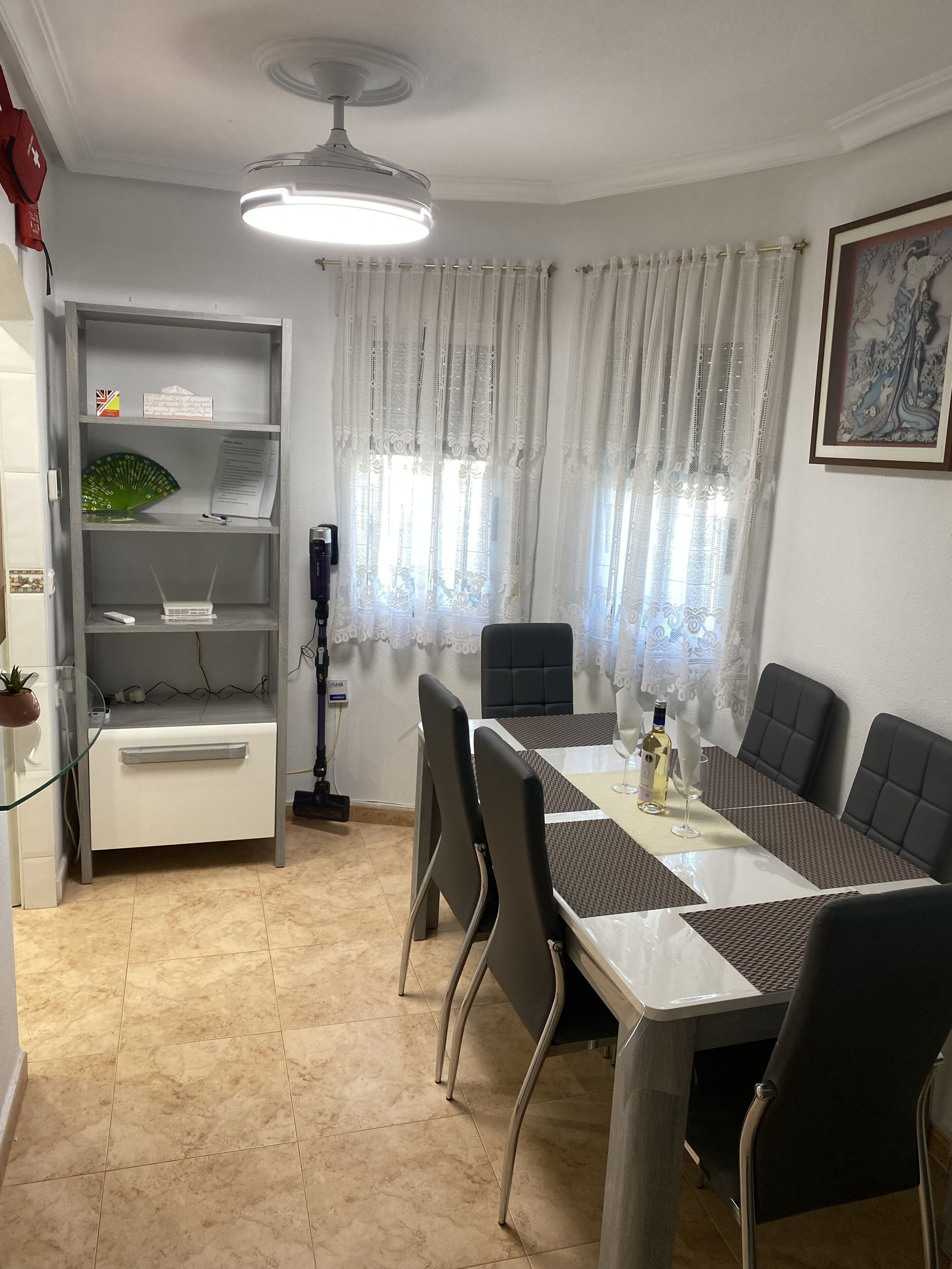 Comedor con una mesa dispuesta para seis personas, rodeada de sillas y un ventilador de techo.
